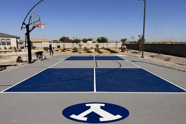 Grey and navy backyard court with a custom logo at center, adjustable hoop and light pole