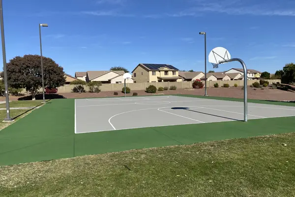 Grey full court on a green surround with two hoops and light poles, houses behind