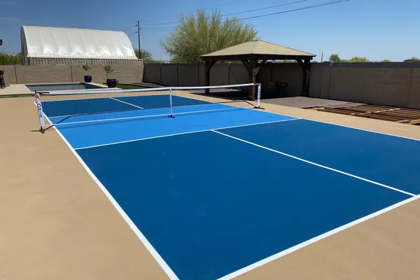 Two-tone blue backyard pickleball court with a net, block wall and gazebo