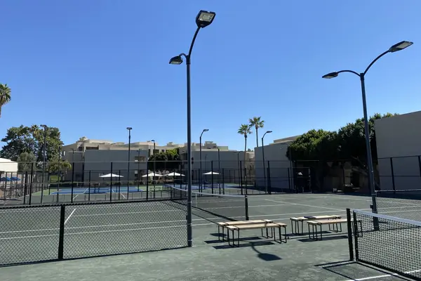 Green club tennis courts with light poles, fencing and benches