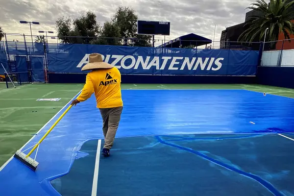 Apex crew member in a yellow Apex shirt squeegeeing blue color coat on a club tennis court
