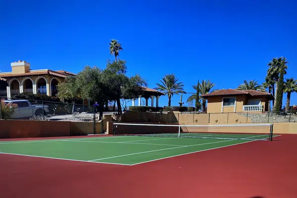 Red and green tennis court in front of a Spanish style home with palms